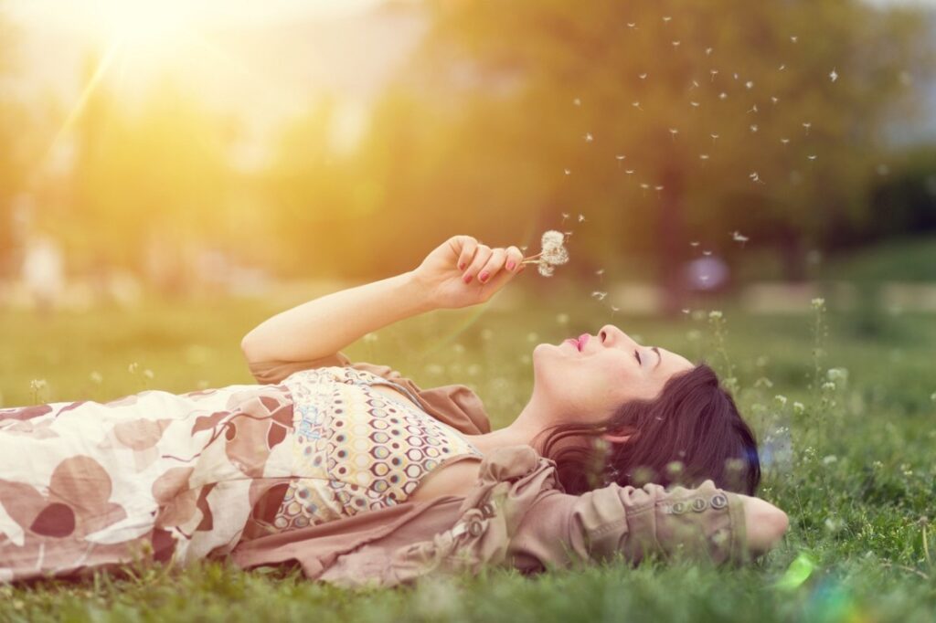 Young woman lying down in the grass and blowing dandelion